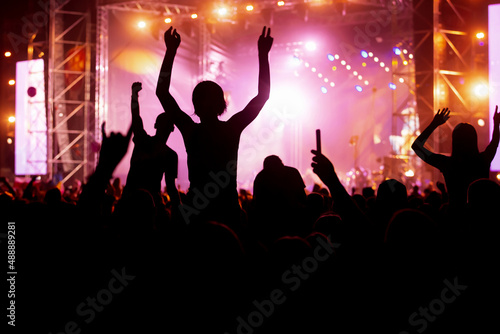 Rock concert, silhouettes of happy people raising up hands.