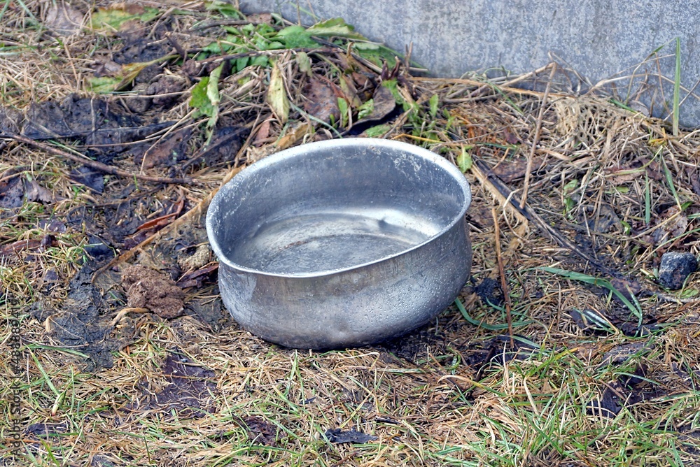 one old gray metal pot of water stands in brown and green grass on the street one old gray metal pot of water stands in brown and green grass on the street