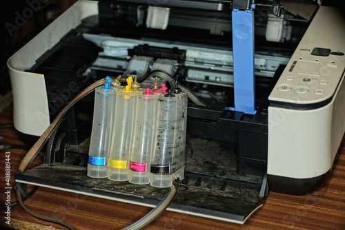 one black open printer with cartridges and a row of empty plastic bottles