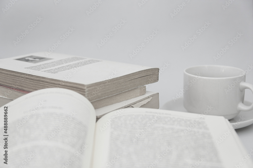 Fototapeta premium Close-up of an open book next to a cup and a stack of reading or study books on white background