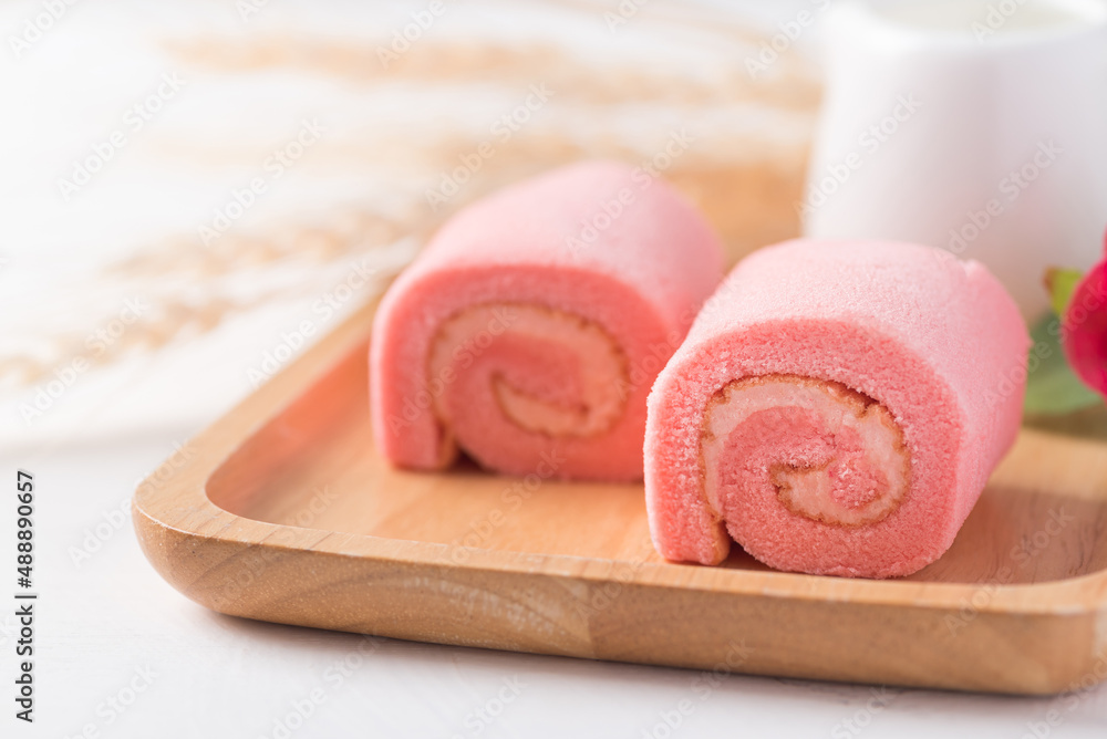 Pink strawberry roll cake or swiss roll with whipped cream and strawberry flavor on wooden plate Pink strawberry roll cake or swiss roll with whipped cream and strawberry flavor on wooden plate
