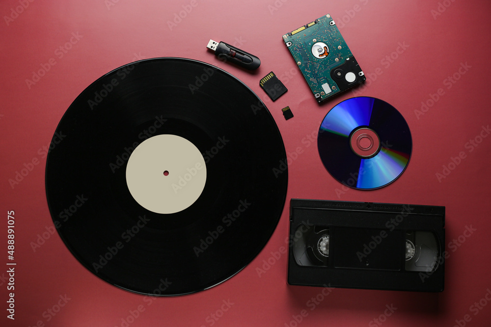 Obraz premium The evolution of recording and storing music and data, vinyl record, cassette, disk, hard drive, flash cards on a red-burgundy background, close-up, top view
