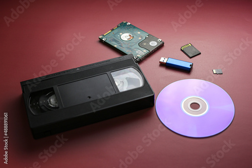 The evolution of recording and storing music and data, vinyl record, cassette, disk, hard drive, flash cards on a red-burgundy background, close-up