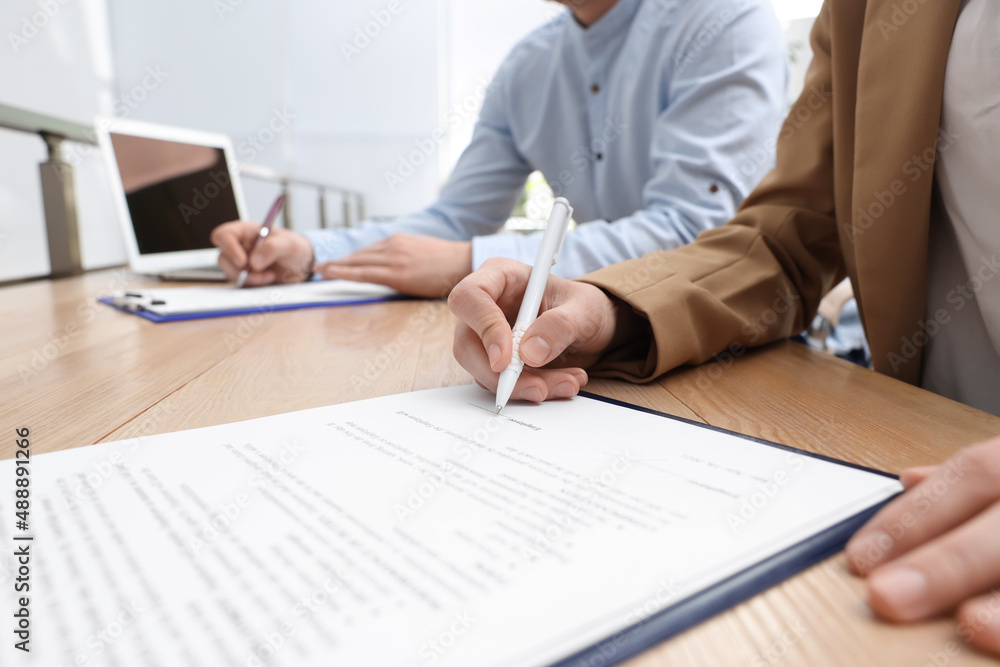 Woman signing contract at table in office, closeup. Woman signing contract at table in office, closeup.