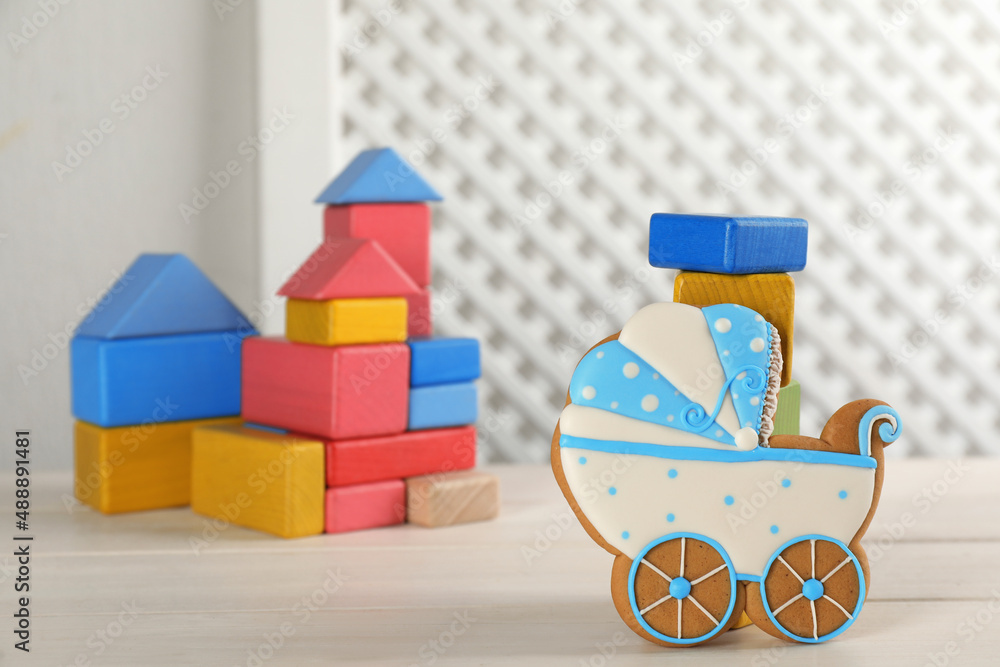 Obraz premium Tasty cookie in shape of stroller and colorful cubes on white wooden table, space for text. Baby shower party