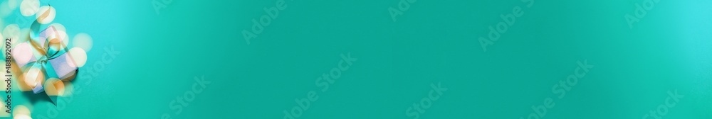 Banner of brown paper gift box with a cyan satin ribbon bow on cyan background with gold bokeh with copy space. Flat lay Happy Birthday father mother day and presents concept Banner of brown paper gift box with a cyan satin ribbon bow on cyan background with gold bokeh with copy space. Flat lay Happy Birthday father mother day and presents concept
