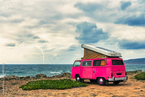 pink clasic camper van standing in front of the sea on a cliff with dramatic sky - travel concept. photo