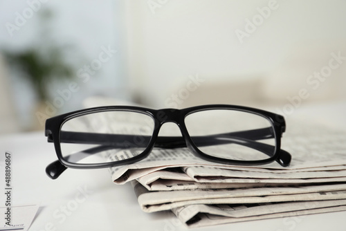 Stack of newspapers and glasses on white table indoors