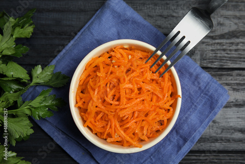 Delicious Korean carrot salad and parsley on black wooden table, flat lay photo