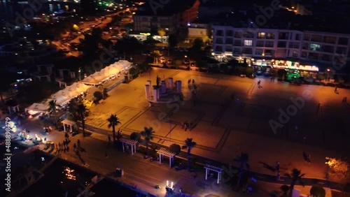 Aerial shot circulating well lit portuary city with palm trees, people walking and boats photo