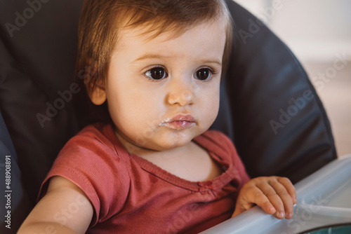 Caucasian baby girl sitting in baby chair with dirty mouth looking away. Baby development. Family concept. Happy face. Family care. Healthy lifestyle concept.