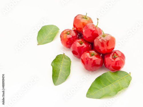 Pile of red acerola cherries and green leaves on a white background