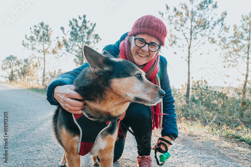 Old woman with his dog during a walk portrait wearing a hat for spring and winter smiling toc amera. Senior people mental health activities outdoors, Active lifestyle on third age. Happy grandma