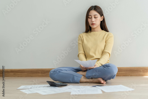 Financial owe asian woman, female sitting on floor home, stressed and confused by calculate expense from invoice or bill, have no money to pay, mortgage or loan. Debt, bankruptcy or bankrupt concept. © KMPZZZ