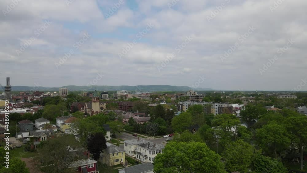 Aerial view with treetops and established city neighborhood with church and newer apartment buildings. Mountains, forest, and river in distance with cloudy sky. Aerial view with treetops and established city neighborhood with church and newer apartment buildings. Mountains, forest, and river in distance with cloudy sky.
