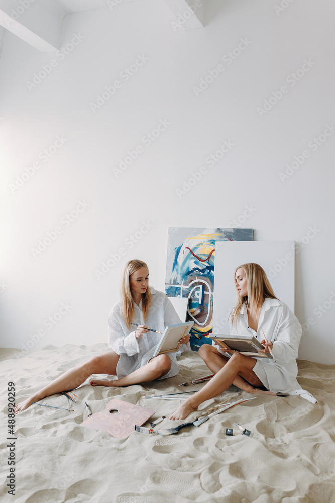 Portrait of happy twin girls artists. Sister girls in a photo studio on the sand.