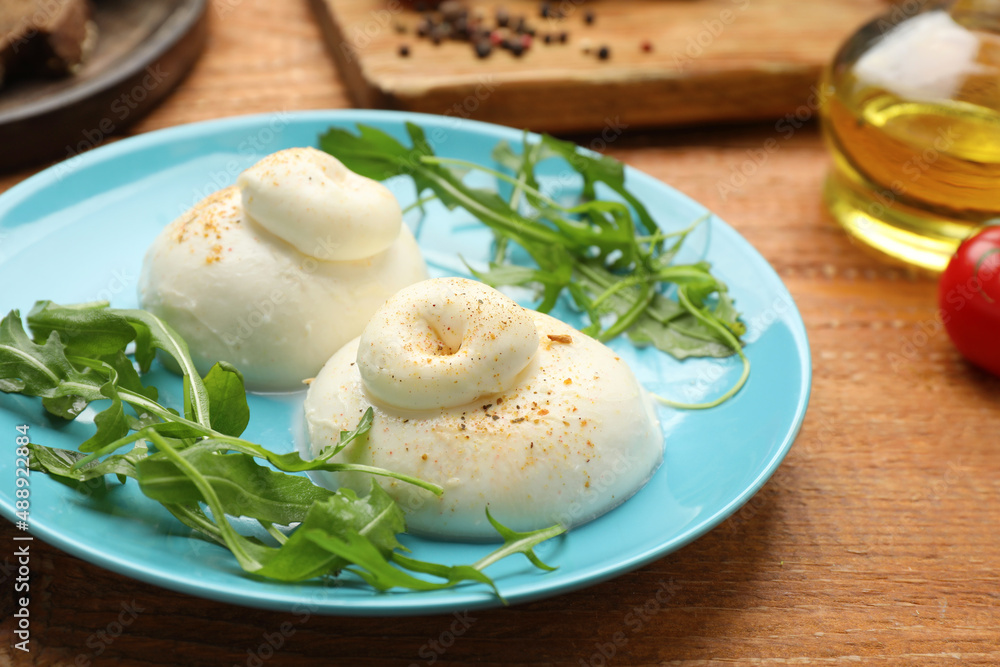 Delicious burrata cheese with arugula on wooden table, closeup Delicious burrata cheese with arugula on wooden table, closeup