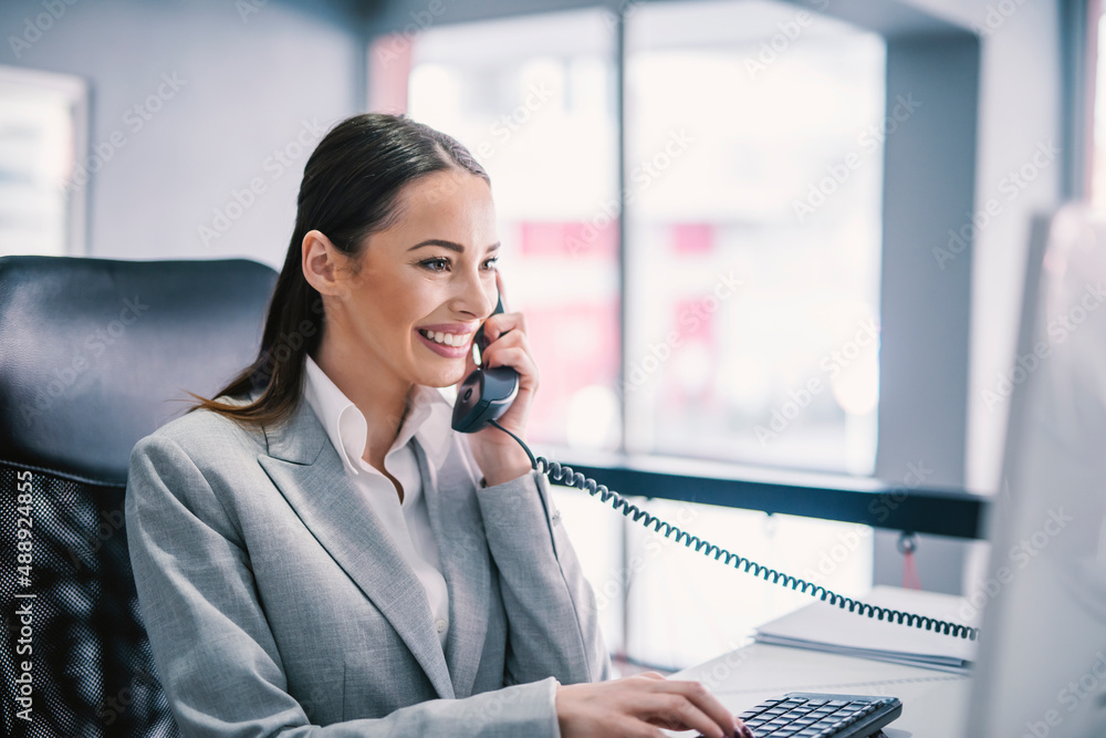 A female entrepreneur typing on keyboard, having phone call and multitasking at office. A female entrepreneur typing on keyboard, having phone call and multitasking at office.