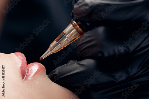 Process applying permanent makeup tattoo of red on lips woman in beautician salon