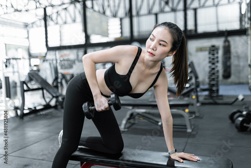 exercise concept The female exercise beginner doing dumbbell workout by resting her left knee and left hand on the bench and raise her right elbow up with a dumbbell in her hand