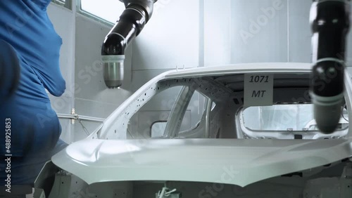 Car body being painted white by robotic arms