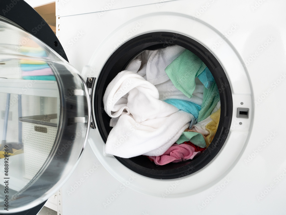 Open front load washing machine and put color clothes before press automatic button for cleaning them in laundry service Open front load washing machine and put color clothes before press automatic button for cleaning them in laundry service