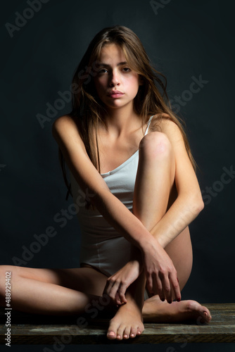 Young model girl with slim body. Portrait of elegant woman with light on a black background. Beautiful female face in the darkness. © Volodymyr