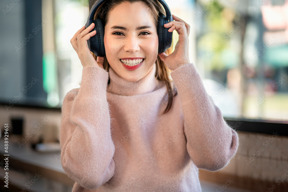 Beautiful Asian girl smiling happily as she listens to music through headphones.