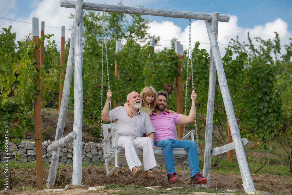 Family men weekend. Three generations of men together, portrait of smiling son, father and grandfather swinging on the swing, having fun in the park outdoor. Family men weekend. Three generations of men together, portrait of smiling son, father and grandfather swinging on the swing, having fun in the park outdoor.