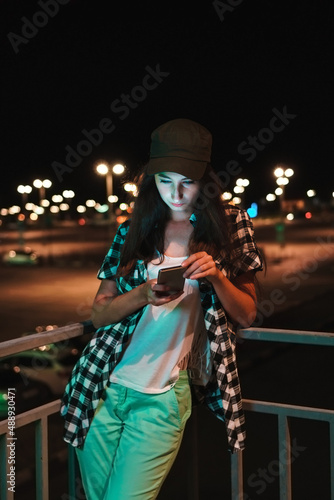 Woman with smartphone on background of car park. Girl on street in evening time. Night life concept.