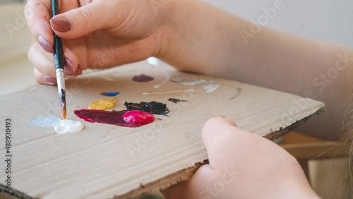 Woman mixes paints with brush on cardboard palette. Preparing for drawing lesson, close up, selective focus.