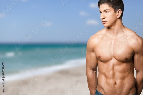 Sexy portrait of muscular handsome topless male model at the beach background.