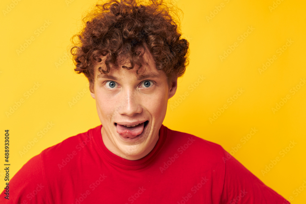 Young curly-haired man red t shirt fun posing casual wear yellow background unaltered Young curly-haired man red t shirt fun posing casual wear yellow background unaltered