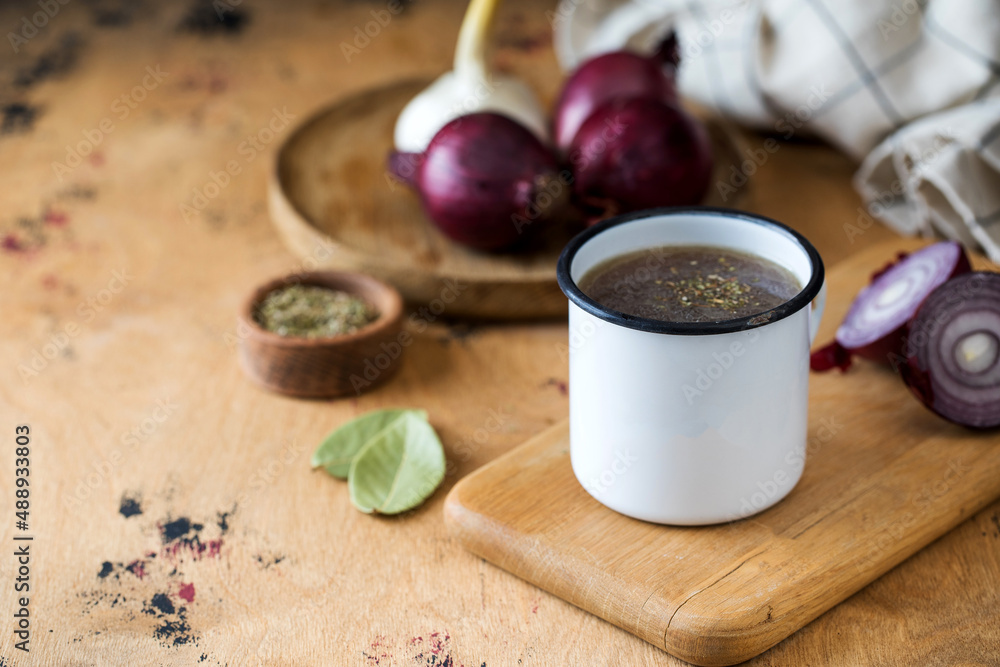 Homemade healthy bone broth with spices in a white mug on a wooden board. Homemade healthy bone broth with spices in a white mug on a wooden board.