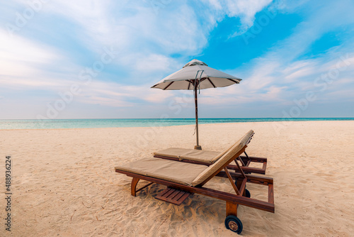 Beautiful tropical sunset scenery  two sun beds  loungers  umbrella. White sand  sea view with horizon  colorful twilight sky  calmness and relaxation. Inspirational relaxing beach coast resort hotel