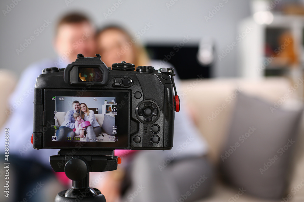 Camera stand on tripod with picture preview on screen, family posing on couch with kid
