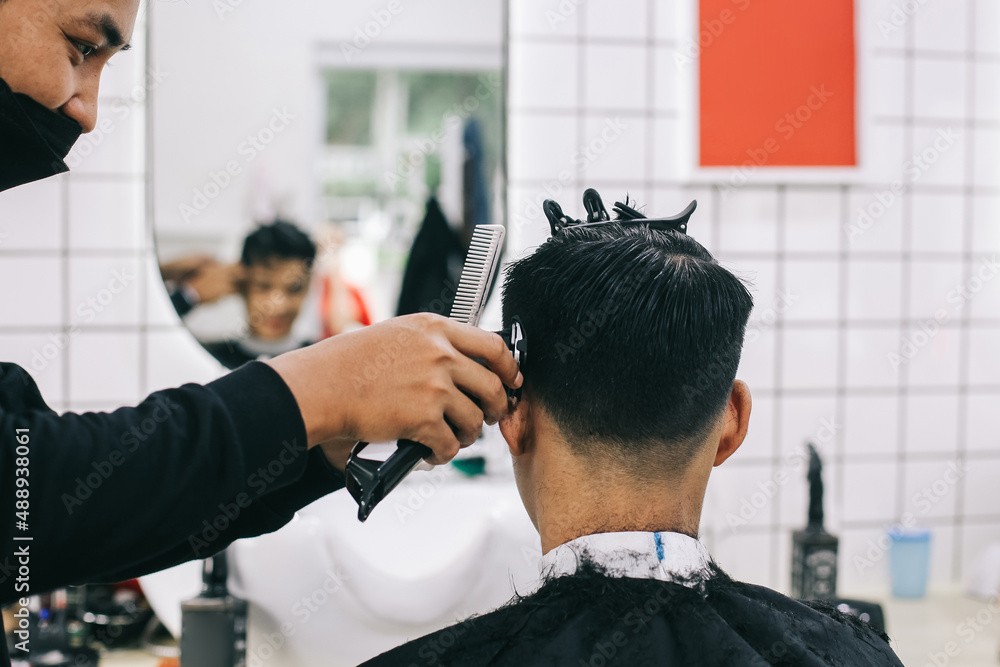 Back view of hairdresser shaving consumer's hair with clipper. Back view of hairdresser shaving consumer's hair with clipper.