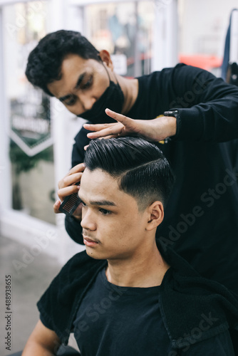 Young man at the barbershop. Hairdresser styling his client's hair in men's hair salon. Self care, masculine beauty. Barber.