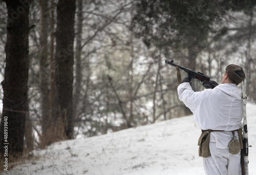A soldier in a winter camouflage coat shoots into the air from a World War II submachine gun. Military historical reconstruction. A shot in the air.