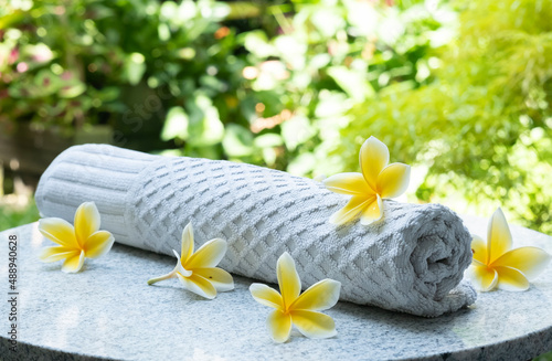 Rolled white towel with yellow frangipani flowers. Spa setting decorated. Side view.