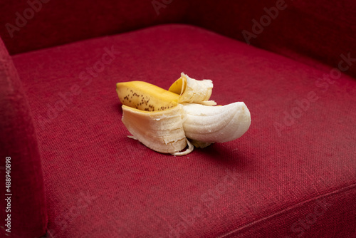 Half peeled ripe banana on dark red sofa. Men's health concept.