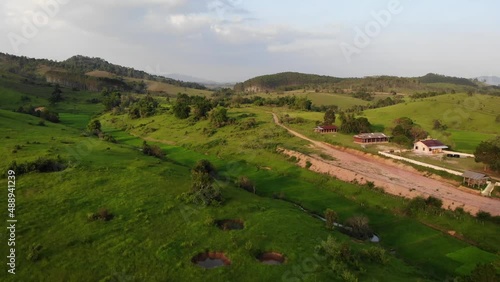 Drone dolly in over a few buildings and dirt road at Muang Souy, Laos. Beautiful rolling hills and green vegetation surrounding. photo