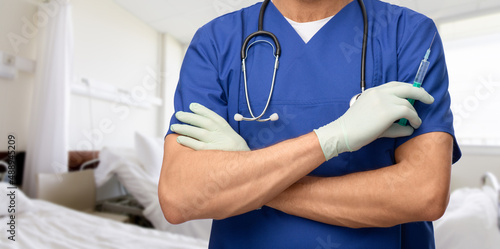 healthcare, vaccination and medicine concept - close up of doctor or male nurse in blue uniform and protective medical gloves with stethoscope and syringe over hospital ward background © Syda Productions