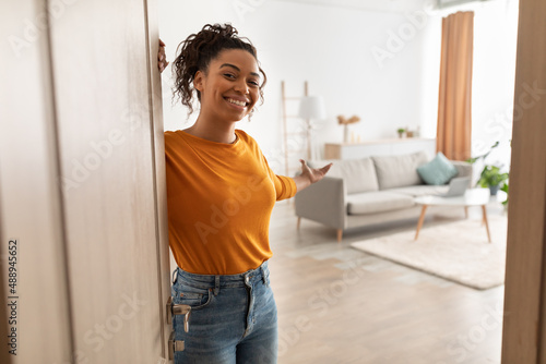 Cheerful African Woman Opening Door Welcoming You Standing At Home photo