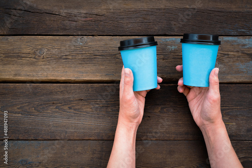 Two coffee cups in female hands on the wooden flat lay background with copy space.