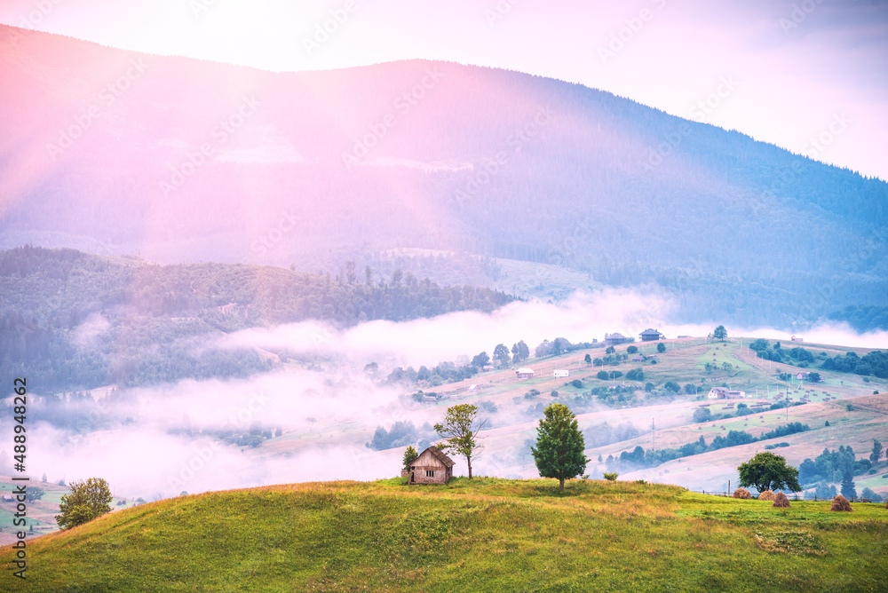 Fototapeta premium Wooden house on a grassy hill in a foggy valley