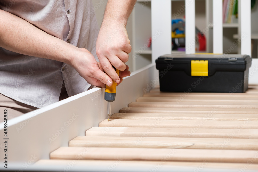 The furniture assembler assembles the bed, twists the screws on the wooden slats, hands with a close-up screwdriver The furniture assembler assembles the bed, twists the screws on the wooden slats, hands with a close-up screwdriver