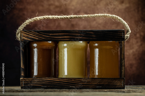 Collection of jars of different types of honey, light, dark and cream, Composition with three jars of honey in a wooden box