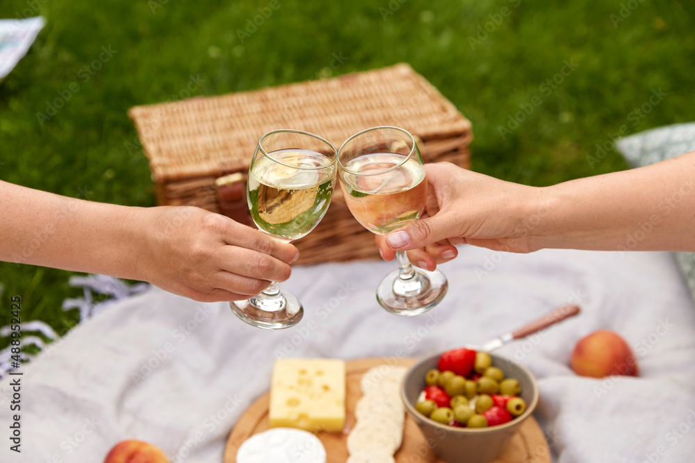leisure, food and drinks concept - close up of hands hands clinking wine glasses above picnic blanket at summer park
