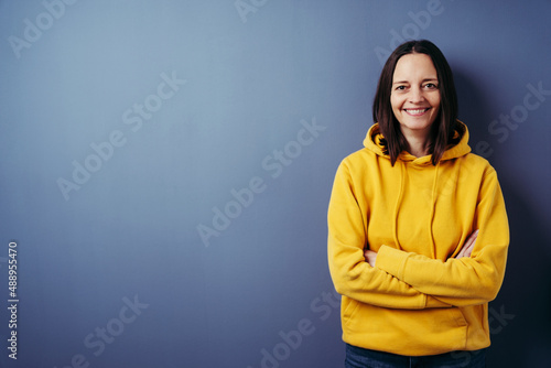 Portrait of smiling woman standing with arms crossed against blue background © contrastwerkstatt